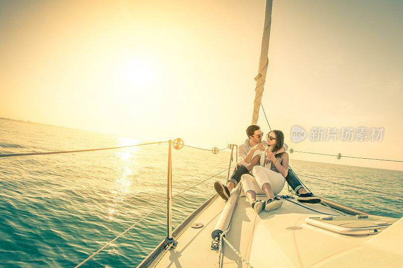日落时分，年轻的情侣在帆船上喝着香槟相爱