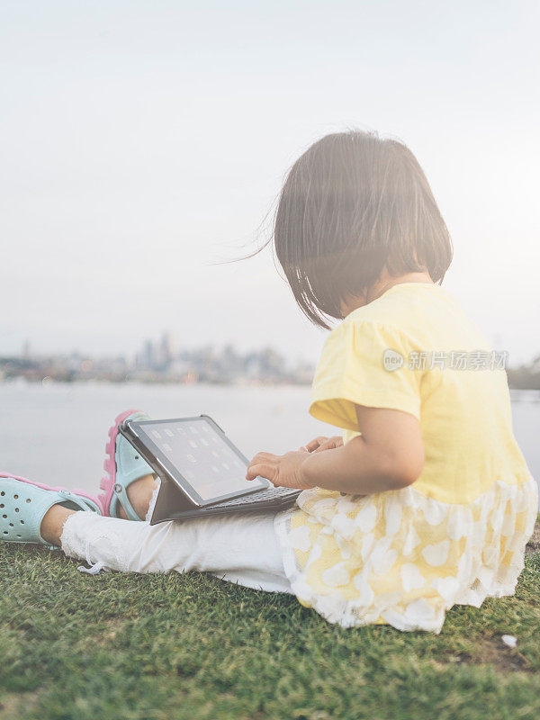 亚洲小女孩坐在草坪上使用平板电脑