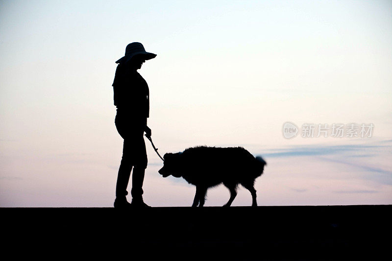 成熟的西班牙妇女和牧羊犬剪影日落