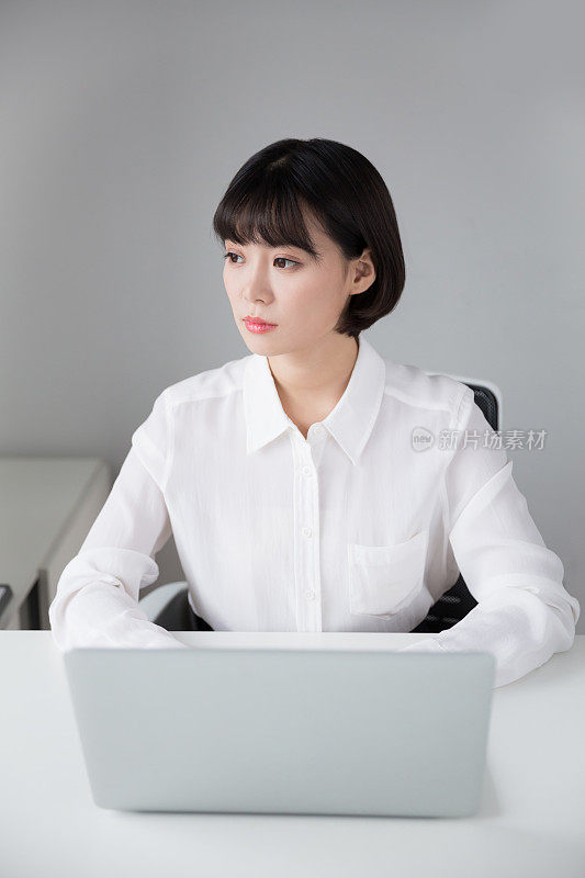 漂亮的中国女孩坐在办公室里用笔记本电脑