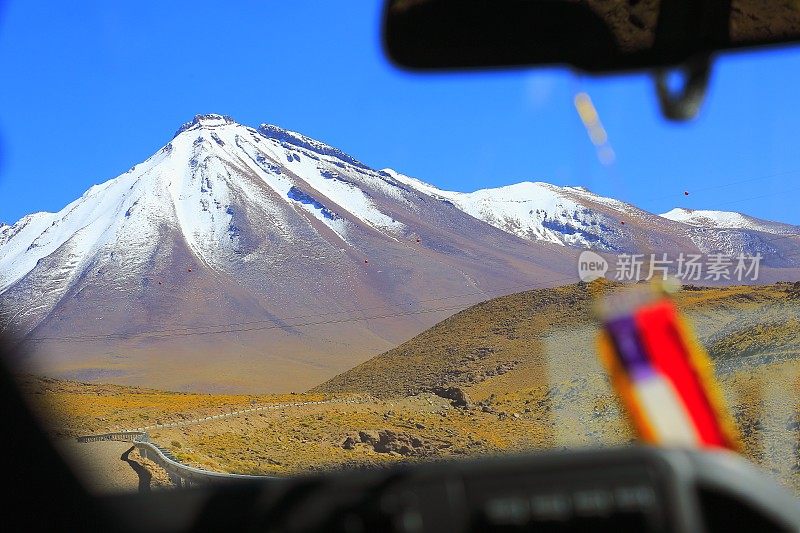 在充满戏剧性的风景的乡村道路上的智利国旗的汽车:雪顶火山和田园般的阿塔卡马沙漠草原，火山景观全景-圣佩德罗阿塔卡马，智利，Bolívia和阿根廷边境