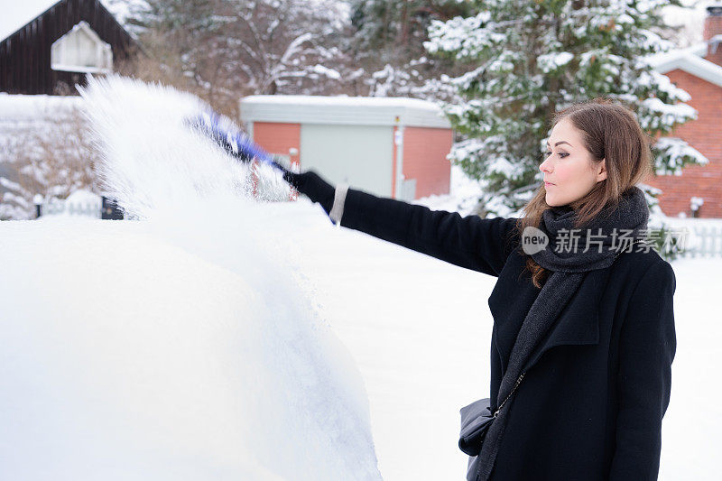 冬天即将来临。女人在冰冷的天气里，车被雪覆盖着。
