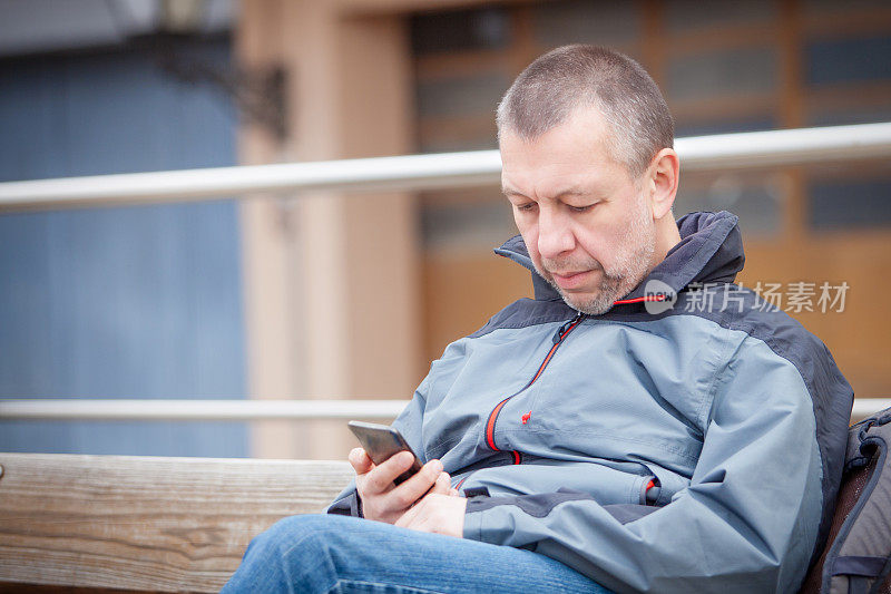 成熟的男人在长凳上看手机