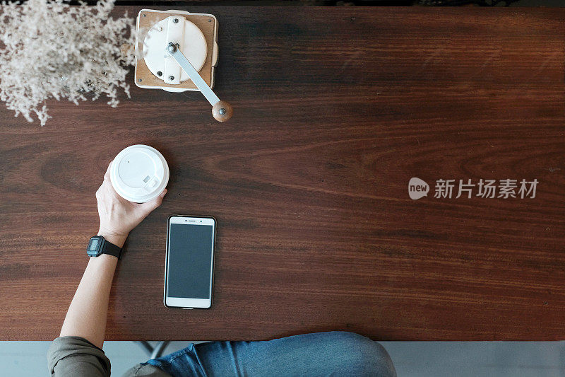 手持咖啡杯和智能手机在木桌的背景下，顶视图与拷贝空间，生活方式，科技