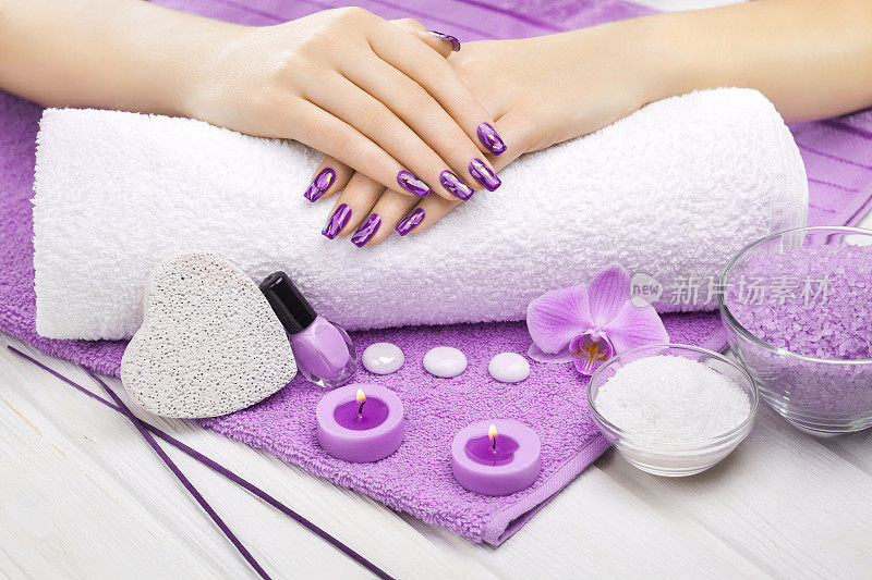 美丽的紫色指甲与兰花，蜡烛和毛巾在白色木制桌子上。
