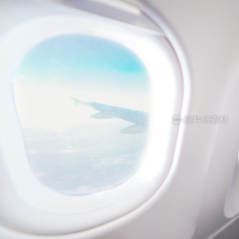 飞机内部的飞机窗口视图。飞机的窗口。度假目的地的概念。浅蓝色的座位和白色的内部与天空和机翼的视野