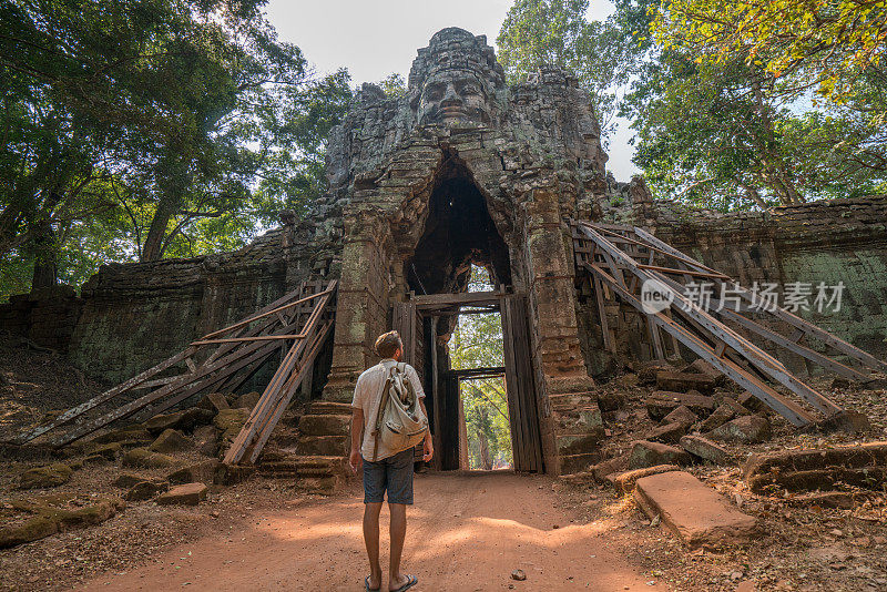 旅游的男游客站在寺庙复杂的大门前仰望上面的雕塑，人们发现探索的概念