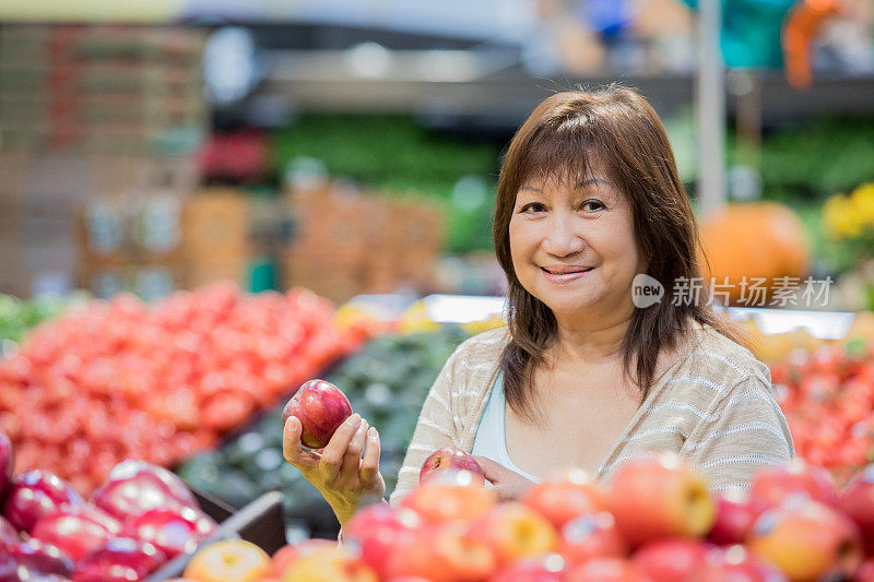 年长亚洲妇女选择新鲜水果在杂货店的农产品区