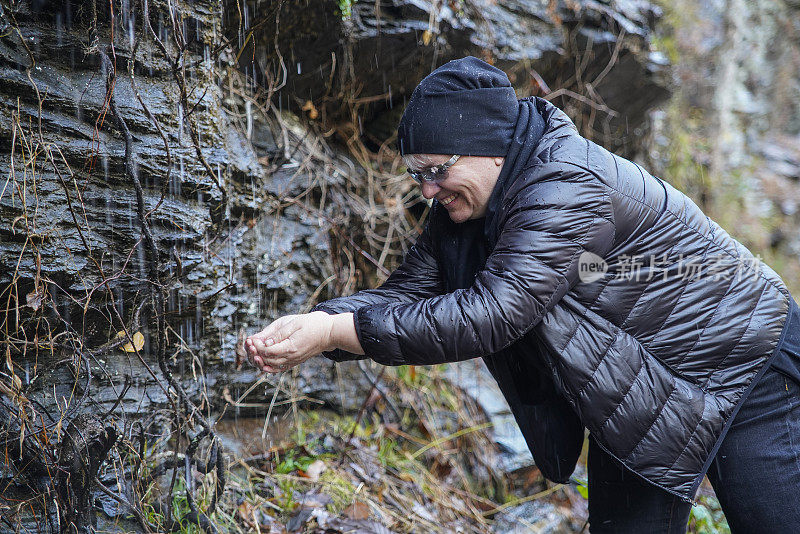 这位成熟的女性，游客，用山上小瀑布的天然水洗脸洗手。