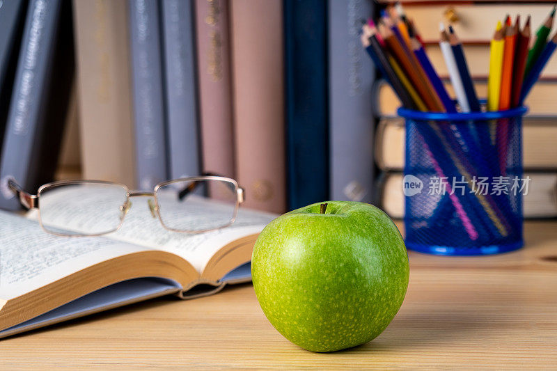 回到学校。书，绿苹果，铅笔和眼镜放在木桌上