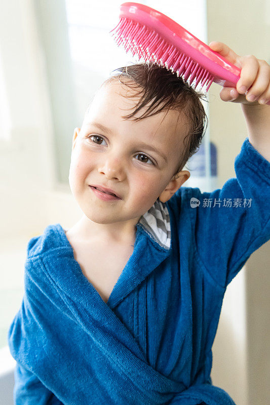 微笑的三岁男孩在浴缸里梳理他湿漉漉的头发