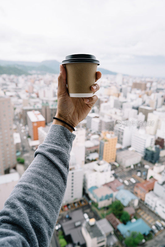 一个男人在他面前举着一个咖啡杯，城市在他的背景