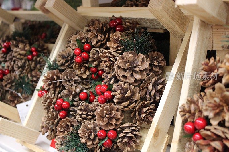 装着圣诞花环的木箱、人造云杉针、干松球果和塑料红冬青浆果的图片，这些都是出售的季节性装饰品