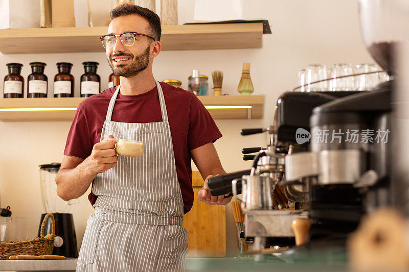 兴高采烈的咖啡师站在咖啡机旁，端着一杯咖啡