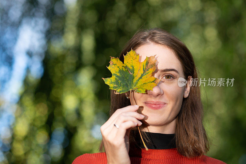 一个年轻女子举着一片落叶挡在眼前