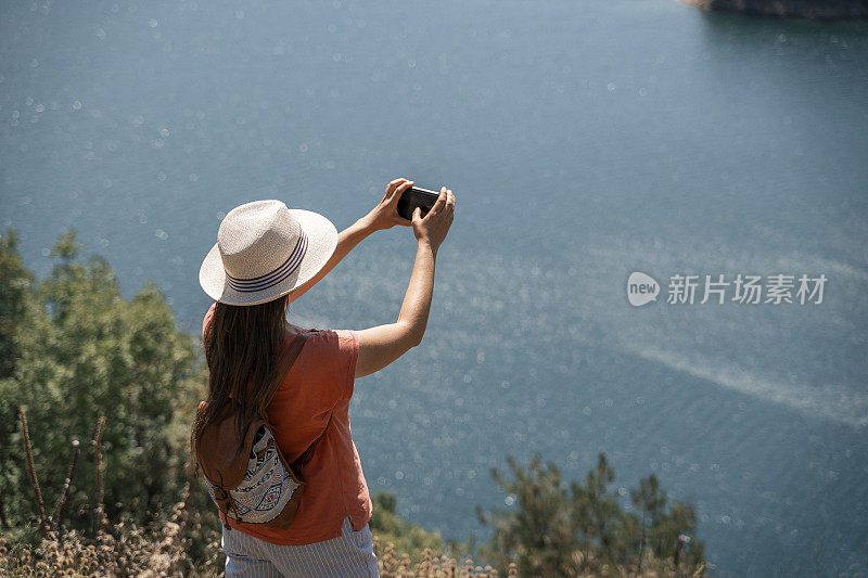 回归自然。一个人用智能手机拍照。一个快乐的年轻女游客漫步在大自然中。阳光明媚的户外享受。