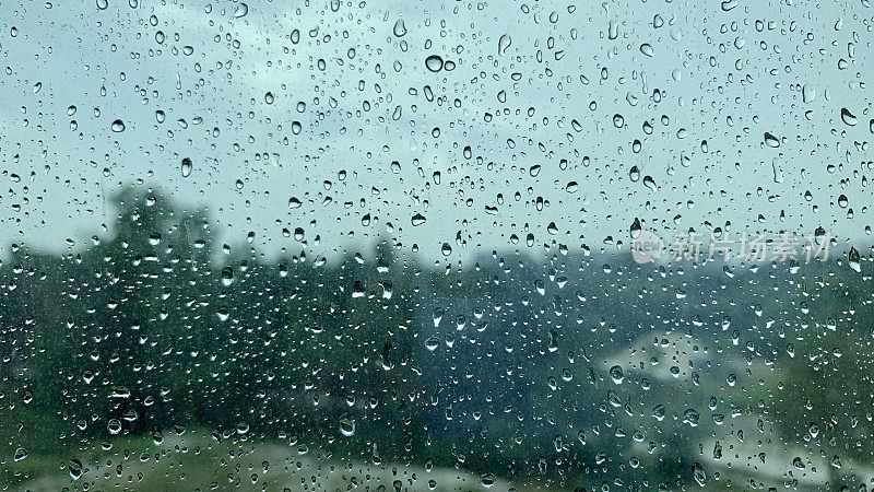 雨点落在窗外的玻璃上，背景是热带树木