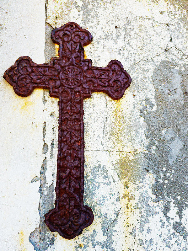 锈迹斑斑、无人照管的旧金属十字架挂在破旧的墙上