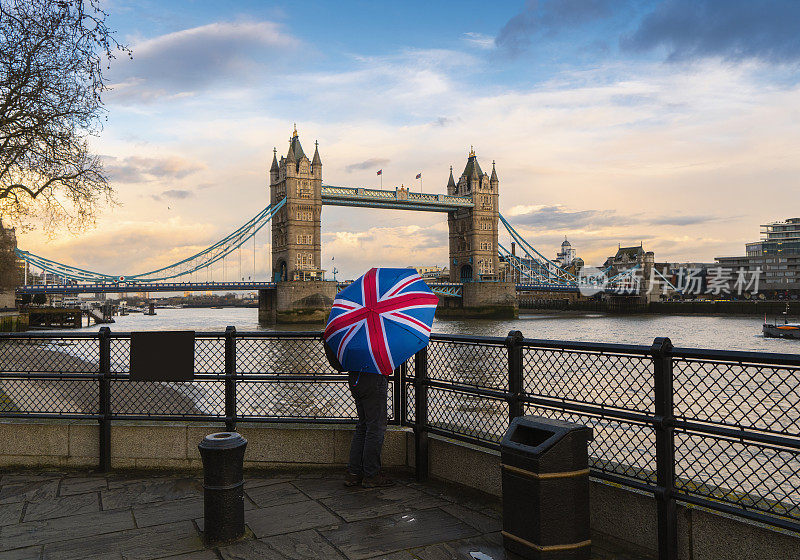 一名游客拿着英国国旗伞在伦敦塔桥上看日落