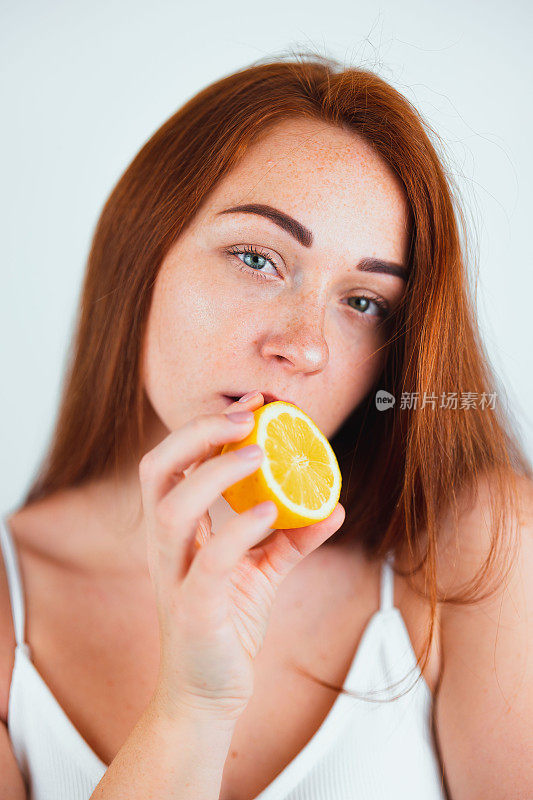 肖像红发年轻女子看起来感性站在孤立的白色背景拿着一半的橙色在她的嘴唇附近，美丽肖像的概念