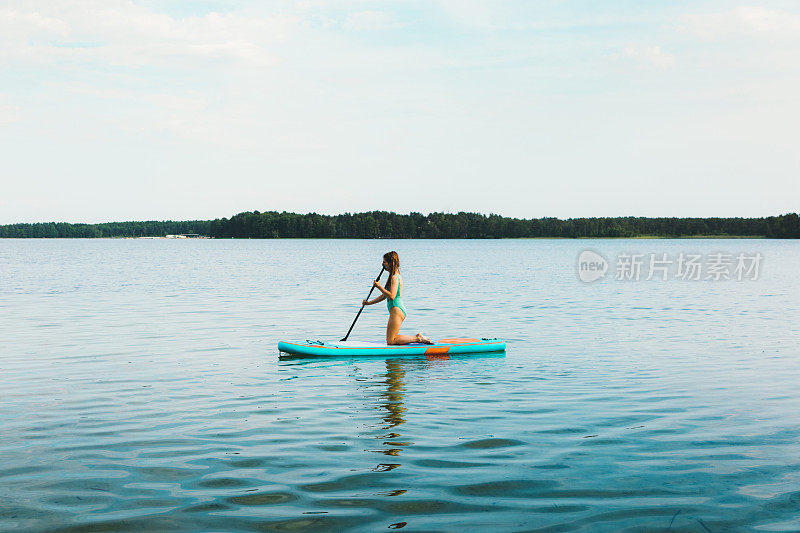 年轻女子欣赏美丽的夏日日落在湖上划水