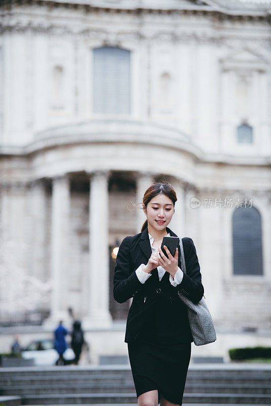 商业上的概念。成功自信的年轻亚洲女商人在伦敦市中心用智能手机查看商业计划