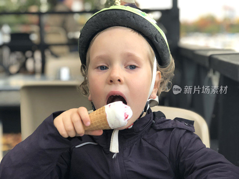 一个拿着华夫蛋筒冰淇淋的女孩的肖像。一个孩子在外面的咖啡馆里津津有味地吃着冰淇淋。