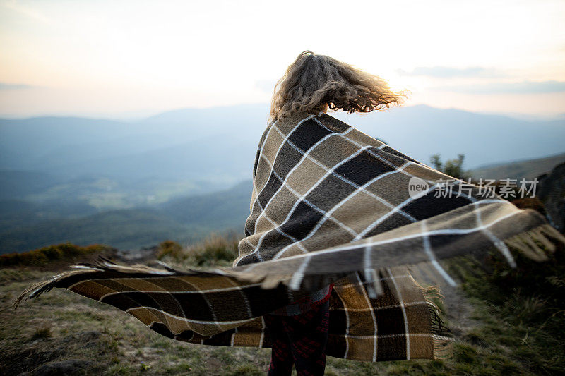 一个漂亮的年轻白种女人正披着花格毯子在秋日的群山中漫步。积极情绪