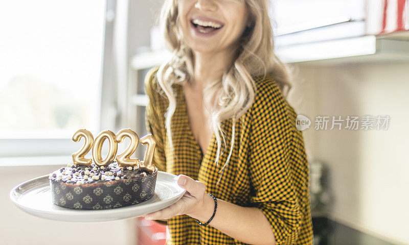 年轻女子制作和装饰巧克力蛋糕与点燃的蜡烛形状的数字2021新年派对的特写