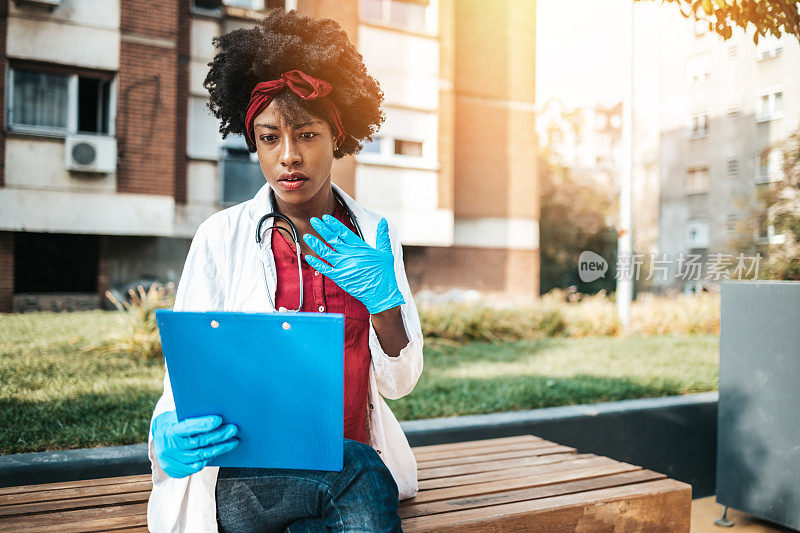 年轻的美国黑人女医生在医院大楼前休息一天的辛苦工作。