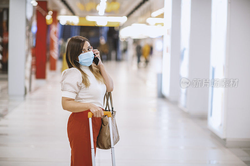 年轻女子戴着防护面罩在机场用手机打电话