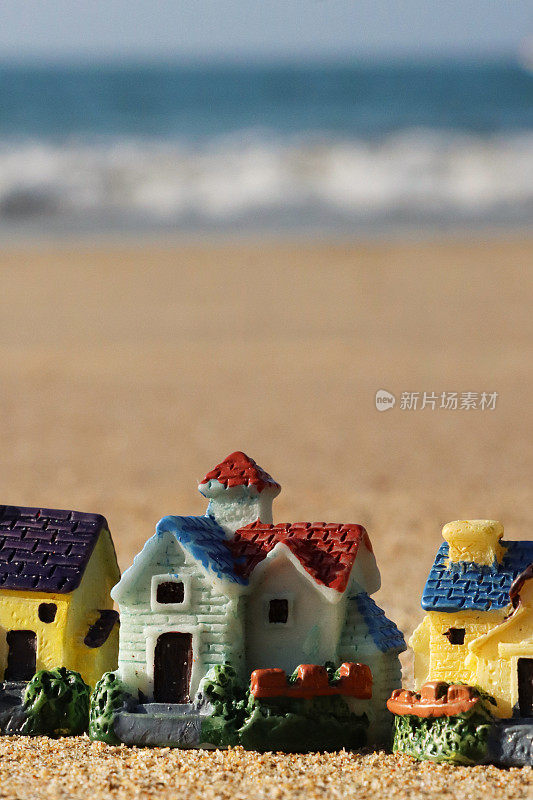 一排模型度假小屋的特写图像，坐落在阳光明媚的沙滩上，背景是退潮时的海浪，大海和海岸线，度假租赁和度假屋的概念，重点放在前景，复制空间