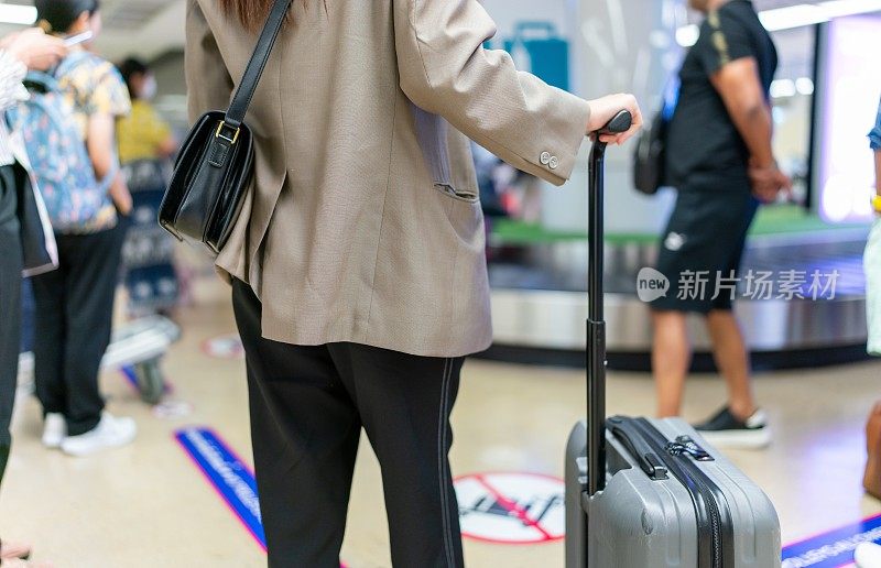 年轻的亚洲女商人在机场行李提取处等候行李