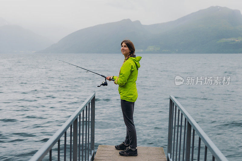 身穿绿夹克的女子在挪威峡湾钓鱼