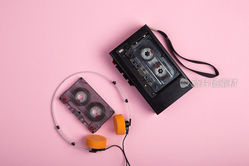 音乐聆听概念。复古盒式磁带，音频播放器和耳机在粉红色背景上的特写，顶视图。