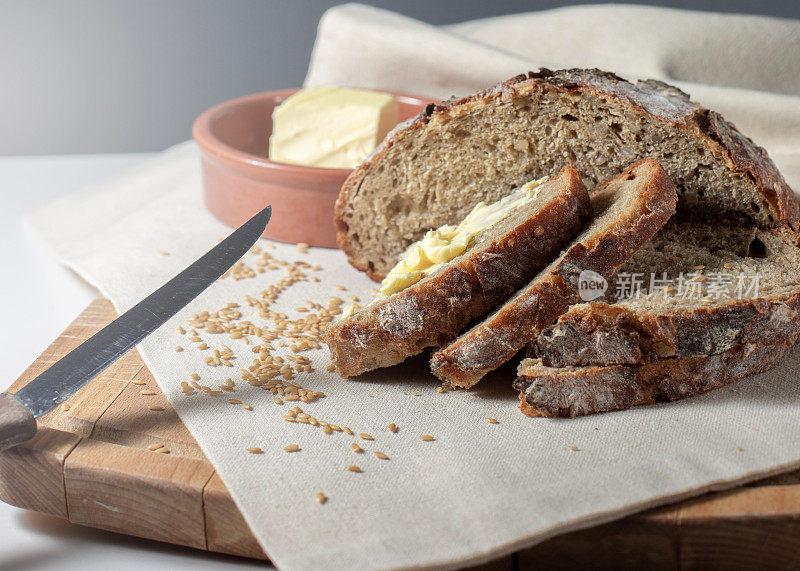 自制烘焙。圆形切片的全麦面包放在木板上，黄油放在陶瓷盘子里，模糊不清。