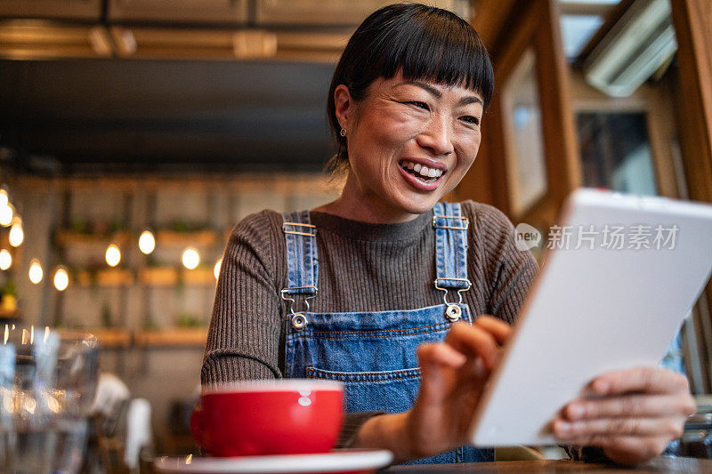 一名日本女子在咖啡馆喝咖啡，用平板电脑与朋友进行视频通话