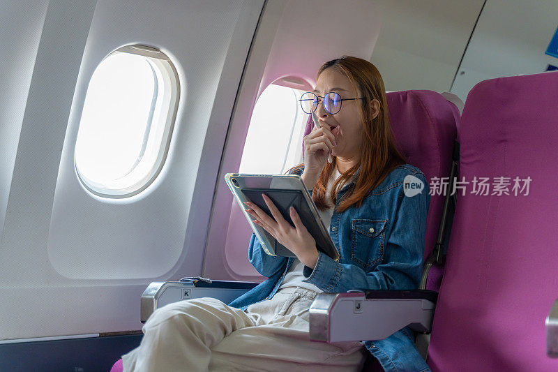 疲惫的年轻女子在飞机上玩平板电脑时打哈欠