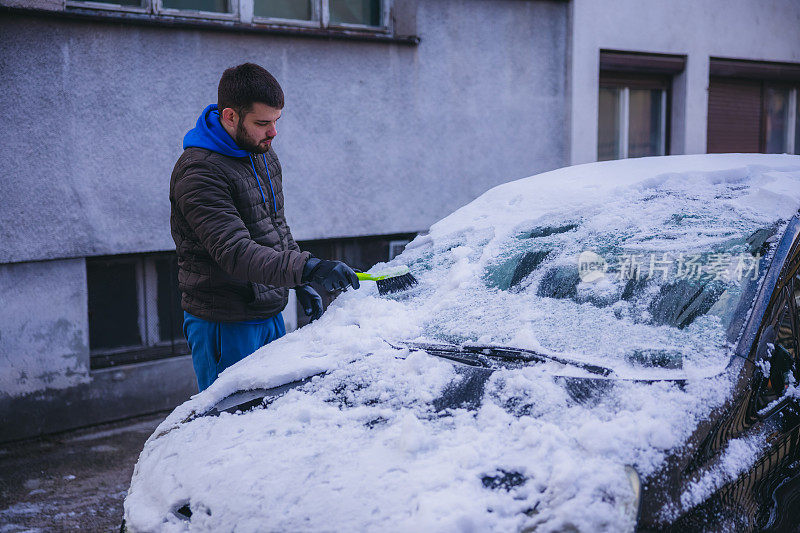 年轻人正在清除汽车上的积雪