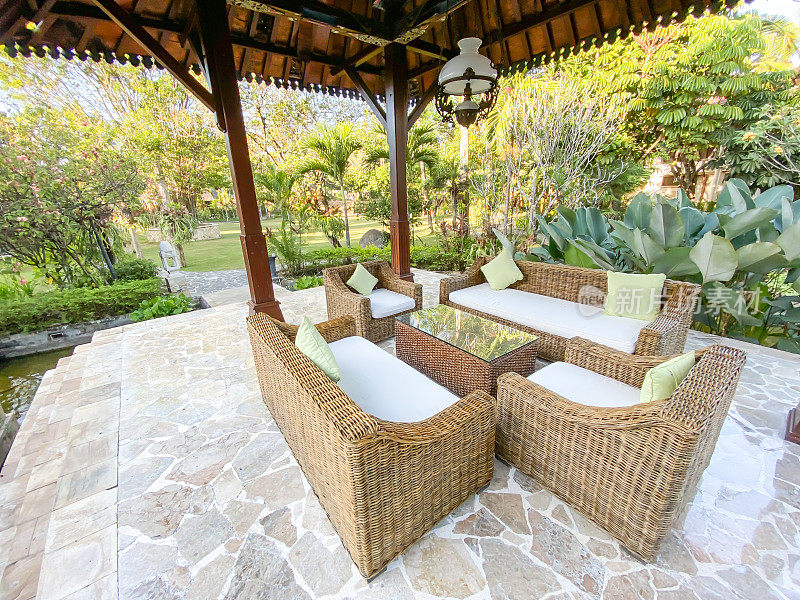 简单的室内酒店大堂，编织藤沙发配白色座椅家具和玻璃桌面，石纹地板，周围有植物。爪哇主题客厅。