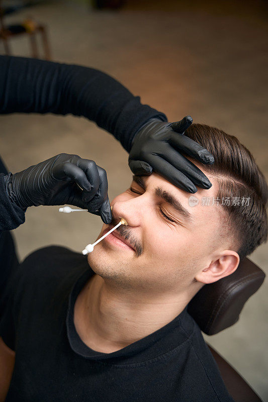 无法辨认的理发师师傅用蜡从男人的鼻子上去除头发