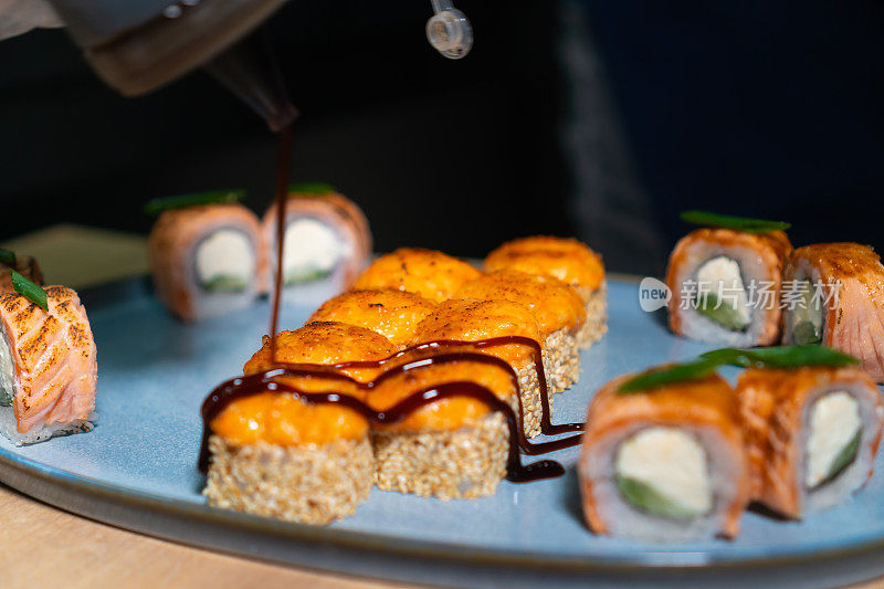 在餐厅的厨房里，厨师把照烧酱倒在盘子里烤好的寿司卷上的特写。