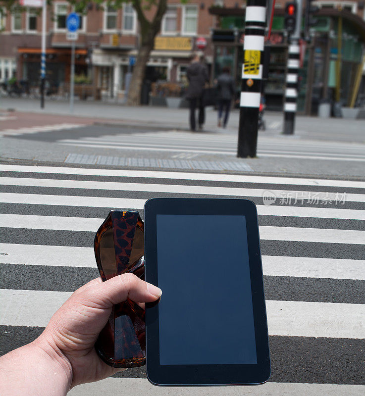 一个女人拿着太阳镜和迷你平板电脑在人行横道上