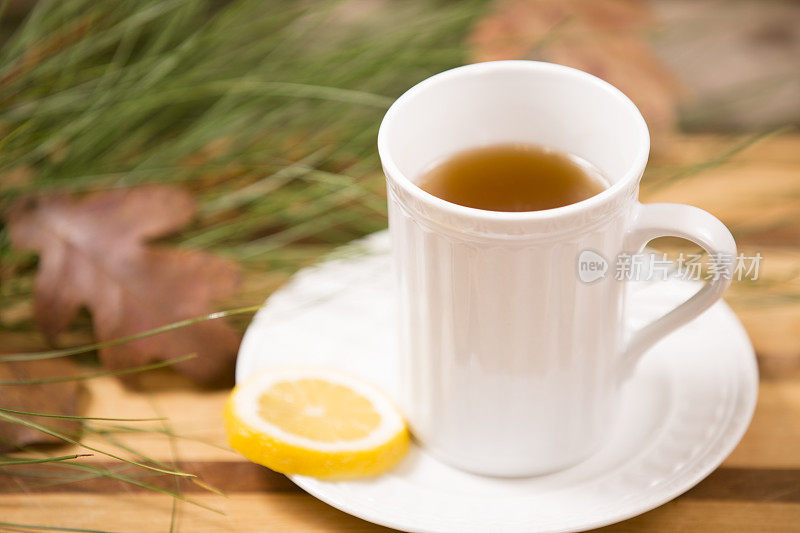 凉茶，白色杯子。落叶，松枝。木制的桌子。