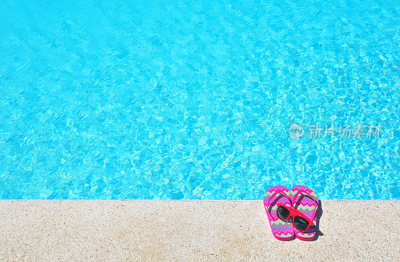 蓝色的游泳池旁边是红色的人字拖和太阳镜