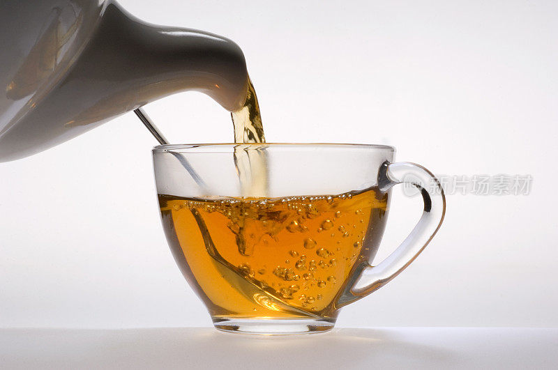 茶水从白色瓷壶倒入玻璃杯中。