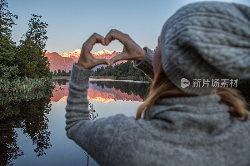 年轻的女子在壮观的山景上做出心形的框架