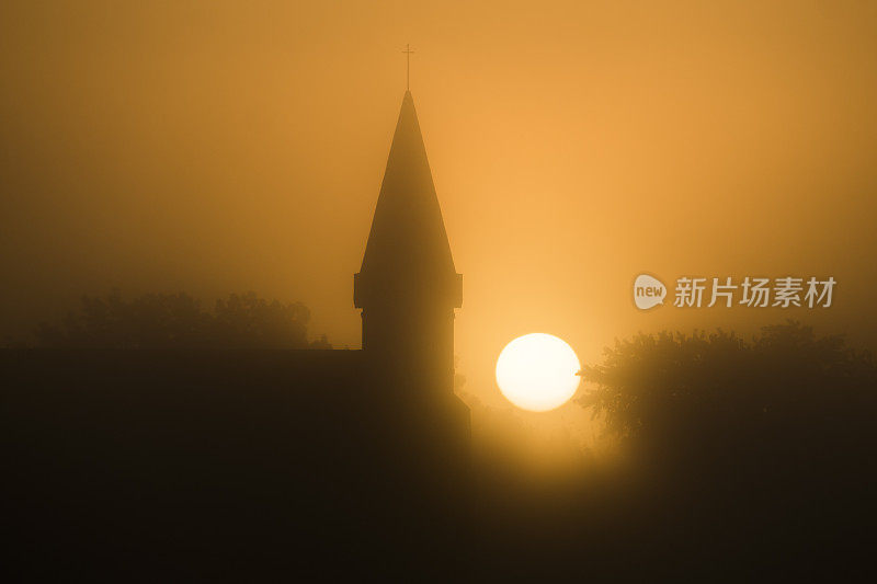 乡村教堂的尖顶在雾蒙蒙的日出中呈现出轮廓。