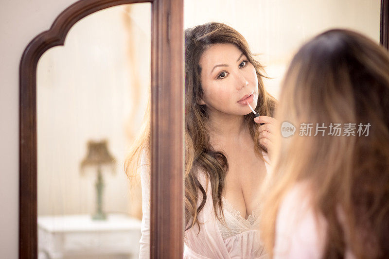 美丽的亚洲女人看着古老的镜子，涂着唇彩