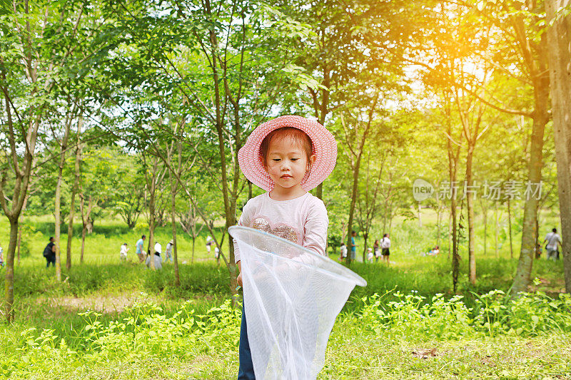 可爱的亚洲女孩戴着草帽和蚊帐在田野里玩夏天。